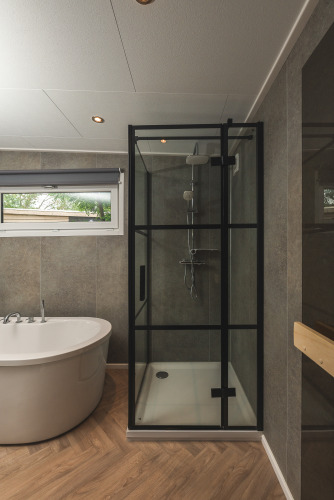 Moderne badkamer bij glamping met vrijstaand bad en glazen douchecabine met zwart frame en houtlookvloer