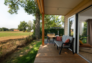 Houten terras van een tiny house met zitbank, tafel en zicht op velden bij Holiday Park Mölke, Nederland.