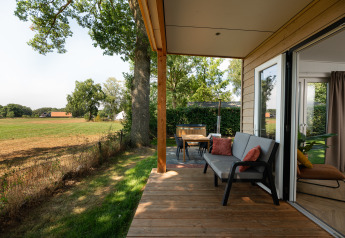 Veranda in legno di una tiny house con divano e tavolo, vista sui campi al Holiday Park Mölke, Paesi Bassi.