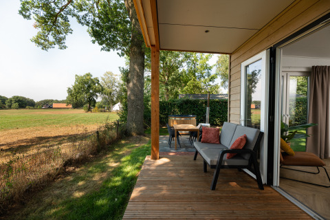 Terraza de madera con sofá y mesa, vistas a los campos en una tiny house del Holiday Park Mölke, Países Bajos.