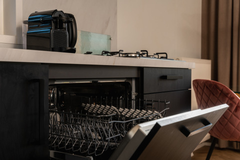 Open dishwasher in a compact kitchen with a coffee machine and stovetop inside a tiny house in the Netherlands.