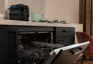 Open dishwasher in a compact kitchen with a coffee machine and stovetop inside a tiny house in the Netherlands.