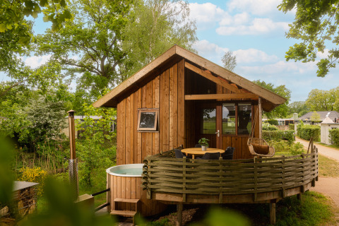 Træhytte kaldet Regge Cottage med udendørs boblebad og terrasse omgivet af grønne træer og natur.