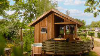 Regge Cottage tiny house with outdoor hot tub and deck, surrounded by lush trees and greenery.
