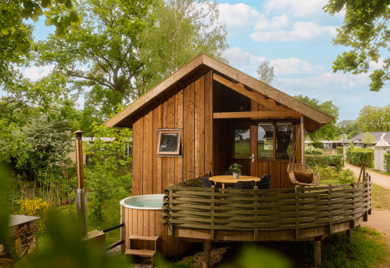 Træhytte kaldet Regge Cottage med udendørs boblebad og terrasse omgivet af grønne træer og natur.