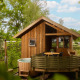 Træhytte kaldet Regge Cottage med udendørs boblebad og terrasse omgivet af grønne træer og natur.
