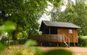 Wooden tiny house called Regge Cottage with porch at Holiday Park Mölke, Netherlands, surrounded by trees.