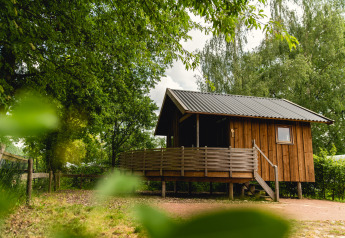 Kleine houten Regge Cottage met veranda in Holiday Park Mölke, Nederland, omgeven door bomen.