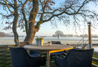 Buitenterras met ronde tafel en vier stoelen, uitkijk op bomen bij Regge Cottage in Nederland.