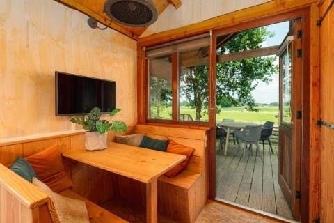 Lys træhytte med spiseplads, tv og udsigt til terrasse og grønne marker i Holiday Park Mölke, Holland.