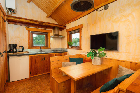 Vista interior del Regge Cottage, una tiny house de madera con zona de comedor, cocina y televisor.