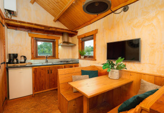 Vista interior del Regge Cottage, una tiny house de madera con zona de comedor, cocina y televisor.