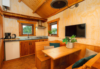 Vista interior del Regge Cottage, una tiny house de madera con zona de comedor, cocina y televisor.