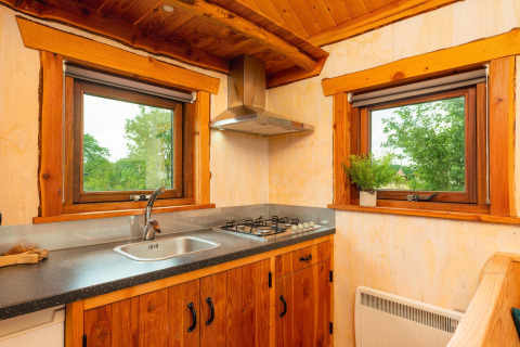 Gemütliche kleine Küche im Regge Cottage mit Holzverkleidung, Gasherd und Blick auf grüne Natur.