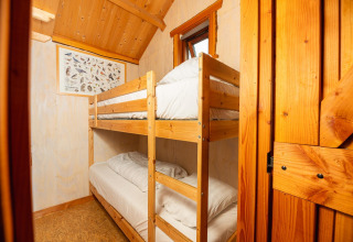 Træhytte med køjeseng og fugleplakat, varmt interiør i Regge Cottage med hems og ovenlysvindue.