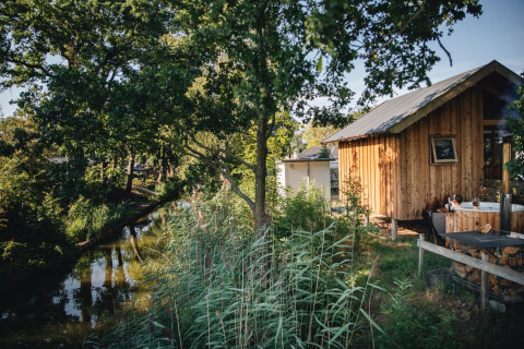 Lille træhytte ved flod, Regge Cottage med spabad i Holiday Park Mölke, Nederlandene, omgivet af natur.