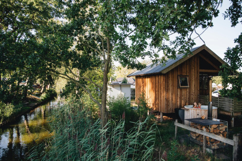 Cozy wooden tiny house by the river with outdoor hot tub at Holiday Park Mölke in the Netherlands.