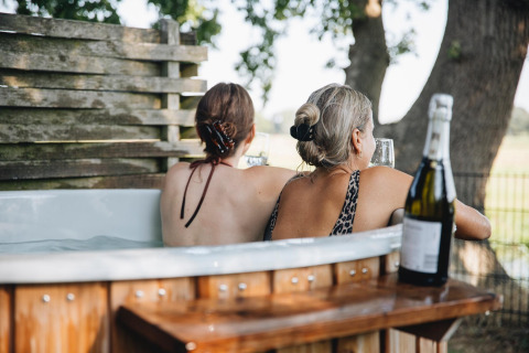 Dos mujeres disfrutan de un jacuzzi con vino en Regge Cottage en Holiday Park Mölke, Países Bajos.