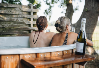 Zwei Frauen entspannen im Whirlpool mit Wein im Regge Cottage im Holiday Park Mölke, Niederlande.
