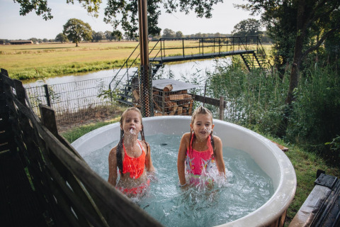 Twee kinderen spelen in een buiten-hot tub bij Regge Cottage, Holiday Park Mölke, met Nederlands landschap.
