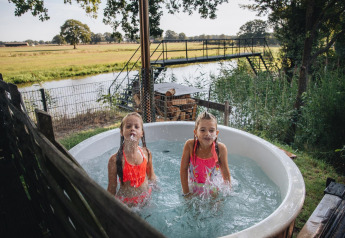 Two kids play in an outdoor hot tub at Regge Cottage, Holiday Park Mölke, with a scenic Dutch backdrop.
