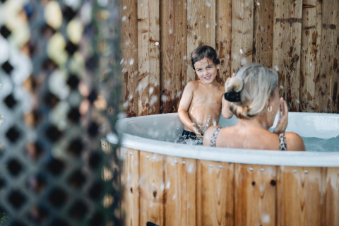 Barn og voksen hygger sig i en udendørs hot tub ved Regge Cottage, Holiday Park Mölke i Holland.