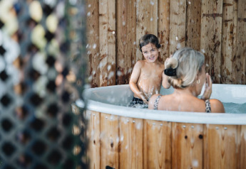 Barn og voksen hygger sig i en udendørs hot tub ved Regge Cottage, Holiday Park Mölke i Holland.