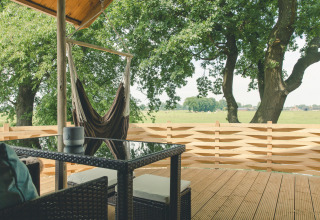 Vue depuis la terrasse de Regge Cottage avec hamac et table, entourée d’arbres au Holiday Park Mölke.