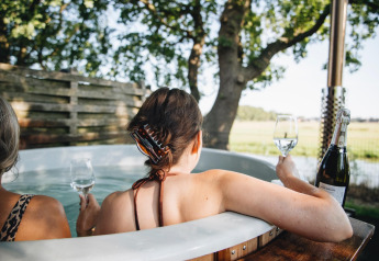 Due donne si rilassano con un bicchiere di vino nella vasca idromassaggio di Regge Cottage, Mölke, Paesi Bassi.