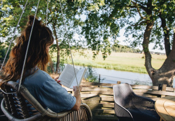 Mujer leyendo un libro en silla colgante en una terraza con vista al río y naturaleza en Holiday Park Mölke.