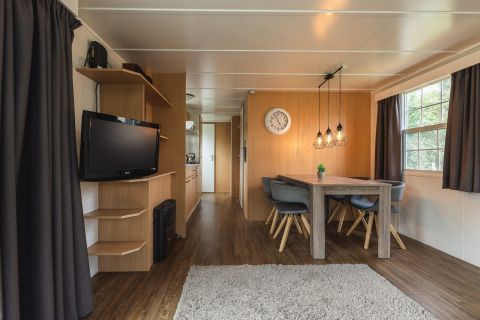 Interior de lodge moderno con mesa de comedor, sillas grises y televisor en Holiday Park Mölke en Países Bajos.