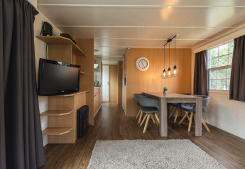 Intérieur de lodge moderne avec table de salle à manger, chaises grises, télé et fenêtres au Holiday Park Mölke.