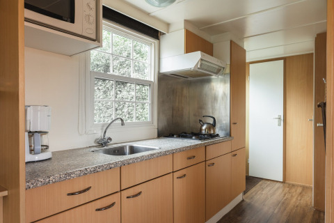Modern kitchen in Bungalette basic + hot tub at Holiday Park Mölke, Netherlands, with wood cabinets and stove.