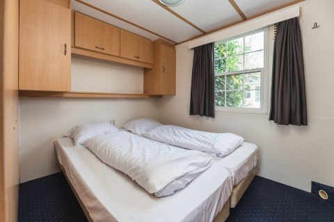 Dormitorio acogedor con cama doble, armarios superiores y ventana en Bungalette basic + jacuzzi en Holiday Park Mölke.