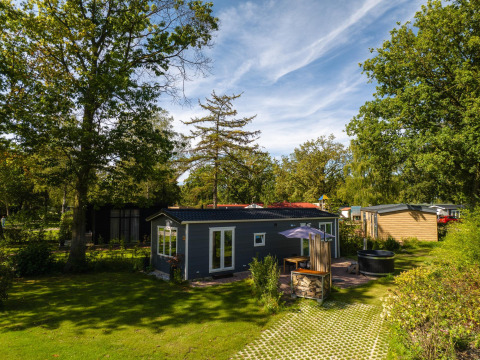 Moderne lodge med boblebad omgivet af grønne træer i Holiday Park Mölke, Nederlandene på en solrig dag.