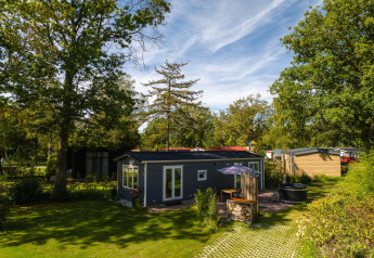 Moderne lodge med boblebad omgivet af grønne træer i Holiday Park Mölke, Nederlandene på en solrig dag.