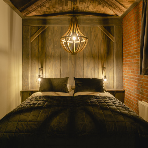 Cama acogedora con ropa de cama oscura y luz cálida en Baby & children bungalow del Holiday Park Mölke, Países Bajos.