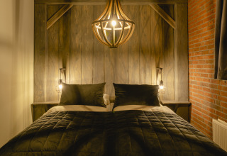 Cozy bed with dark bedding, warm lighting, and rustic wood paneling at Baby & children bungalow, Holiday Park Mölke.