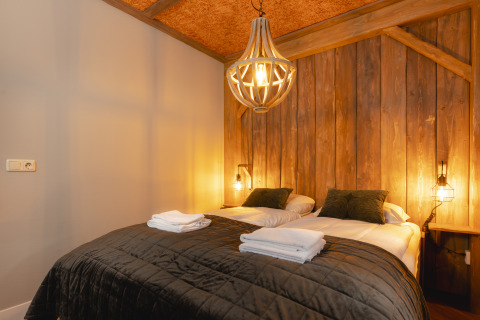 Dormitorio acogedor con cama doble, pared de madera y luz cálida en bungalow apto para niños.