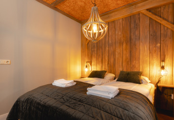 Knusse slaapkamer met tweepersoonsbed, houten wand en warme verlichting in een kinderbungalow.