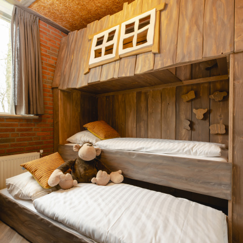 Habitación infantil con literas de madera y peluche de mono en Baby & children bungalow, Holiday Park Mölke.
