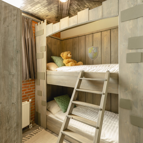 Dormitorio infantil con literas de madera, oso de peluche, cojines verdes y ambiente acogedor en bungalow.