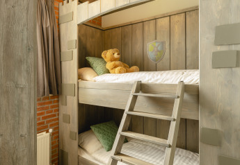 Camera per bambini con letti a castello in legno, orsacchiotto, cuscini verdi e decoro accogliente in un lodge.