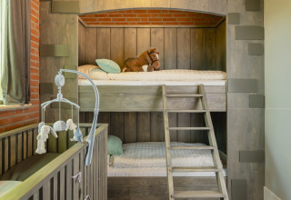 Habitación infantil con litera estilo castillo, cuna y peluche en Holiday Park Mölke, Países Bajos.