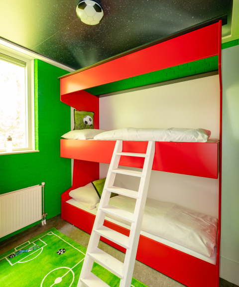 Voetbalthema kinderkamer met stapelbed, groene muren, speelmat en raam in Holiday Park Mölke, Nederland.