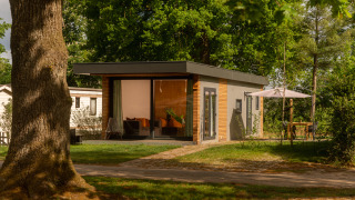 Moderna tiny cabin en Holiday Park Mölke en los Países Bajos, rodeada de árboles y área de descanso exterior.
