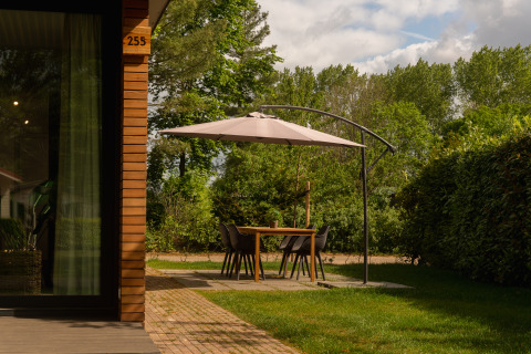 Buiteneethoek met parasol naast een houten tiny cabin bij Holiday Park Mölke, Nederland.