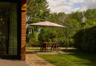 Buiteneethoek met parasol bij een houten tiny cabin in Holiday Park Mölke, Nederland.