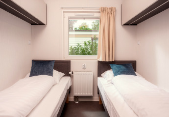 Zwei Einzelbetten und ein Fenster in einem hellen Zimmer der Tiny Cabin im Holiday Park Mölke, Niederlande.
