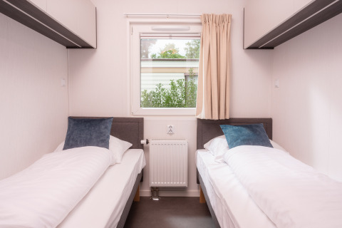 Zwei Einzelbetten und ein Fenster in einem hellen Zimmer der Tiny Cabin im Holiday Park Mölke, Niederlande.